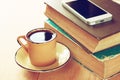 Cup of coffee, stack of old books and smartphone over wooden table, retro filtered image Royalty Free Stock Photo