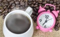 Cup of coffee with steam and pink clock on table with coffee beans background. Concept coffee and time Royalty Free Stock Photo