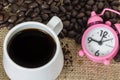 Cup of coffee with steam and pink clock on table with coffee beans background. Concept coffee and time. Royalty Free Stock Photo