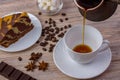 A cup of coffee and a tasty cake on a saucer. Chocolate bar, coffee beans, a bowl with sugar cubes, and anise on bright wooden bac Royalty Free Stock Photo