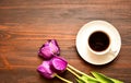 A cup of coffee or tea on a saucer stands on a wooden background, purple tulips lie next