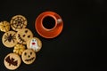 A Cup of coffee, terribly tasty cookies with terrible emoticons, cobwebs, spiders, bats, pumpkins on a black background. Royalty Free Stock Photo