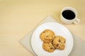 A cup of coffee, three pieces of chocolate chip cookies in a white round dish
