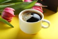 Cup of coffee with tulips and gift box on yellow background, clos Royalty Free Stock Photo