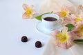 A cup of coffee with two chocolates, daylily flowers on a delicate scarf on a white background, a place for text, a side view-the