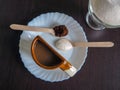 A Cup of coffee with an unusual shape on a white plate and spoons with ground coffee and sugar Royalty Free Stock Photo