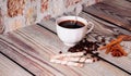 A cup of coffee, waffle rolls, cinnamon, anise and coffee beans lie on a wooden table