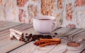 A cup of coffee, waffle rolls, cinnamon, anise and roasted coffee beans lie on a wooden table