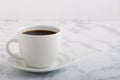 Cup of coffee in white mug on a white plate on top of a marble coutertop Royalty Free Stock Photo