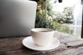 A cup of coffee on the wooden table behide laptop