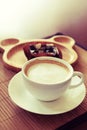 Cup of coffee on wooden table with blur plate of brownie at background.