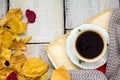 A cup of coffee on wooden table with fallen leaves.