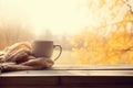 AI generated. Cup of coffee wrapped in cozy scarf and autumn leaves on windowsill with autumn park on window