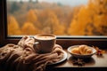 AI generated. Cup of coffee wrapped in cozy scarf on plate with cinnamon, croissant and autumn leaves on window
