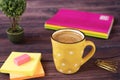 A cup of coffee. Yellow cup of white dots. Around office desk supplies in bright, neon colors - notebooks, gold pins, stickers