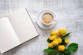 A cup of coffee, yellow peony roses and open book on the white wooden table. Morning ritual.