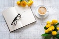 A cup of coffee, yellow roses and open book with glasses on the white wooden table. Top view. Royalty Free Stock Photo
