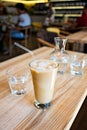 A cup of cold ice coffee with milk and tube to drink in a glass on wooden background with carafe of water. Royalty Free Stock Photo