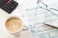 Cup of creamy coffee with tax return form, pen, calculator and glasses on table