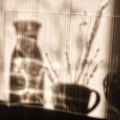 Cup and a decanter of water in the sun. Dark shadows from objects in the kitchen. Kitchen shadows on wooden background