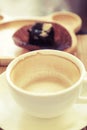 Cup of drinking coffee on wooden table with blur plate of brownie at background.