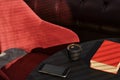 Cup of espresso on a black table, a red book and a red armchair, bright sunbeams on the table. Interior details of a cafe or loft