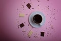 A cup of espresso coffee, pieces and crumbs of chocolate on a pink background.