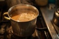 A cup filled with liquid sitting on top of a hot stove, A soothing scene of a pot of masala chai simmering on the stove, AI