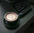Cup of Flat White coffee in a green cup next to an old typewriter on green wood table