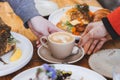 a cup of flat white coffee in cream ceramic cup with latte art on top, touched by two hands, surrounded with variety of food on