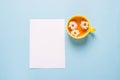 A cup of flowered chamomile tea and a blank empty sheet of white paper on a blue background .