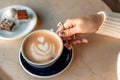 A cup of fresh cappuccino coffee in the hands of a woman on a fashionable background of a white marble table, next to a Royalty Free Stock Photo