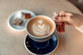 A cup of fresh cappuccino coffee in the hands of a woman on a fashionable background of a white marble table, next to a Royalty Free Stock Photo