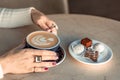 A cup of fresh cappuccino coffee in the hands of a woman on a fashionable background of a white marble table, next to a Royalty Free Stock Photo