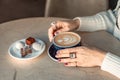 A cup of fresh cappuccino coffee in the hands of a woman on a fashionable background of a white marble table, next to a Royalty Free Stock Photo