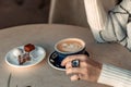 A cup of fresh cappuccino coffee in the hands of a woman on a fashionable background of a white marble table, next to a Royalty Free Stock Photo