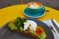 Cup of fresh flat white coffee and delicious toast with avocado and egg Benedict Royalty Free Stock Photo