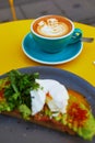 Cup of fresh flat white coffee and delicious toast with avocado and egg Benedict Royalty Free Stock Photo