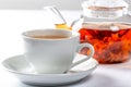 A Cup of fresh tea on a saucer, behind the Tea in a glass teapot with a blooming large flower. Exotic green tea on white Royalty Free Stock Photo