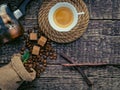 A cup of frothy coffee, a bag of spilled coffee beans and cane sugar lumps on an old wooden surface Royalty Free Stock Photo