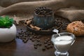 Cup full of coffee beans with plant, bun and milk on brown table Royalty Free Stock Photo