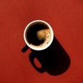 Cup full of coffee with harsh black shadows on a vivid red background