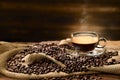 Cup glass of coffee with smoke and coffee beans on burlap sack on old wooden background Royalty Free Stock Photo