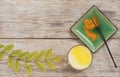 Cup with golden milk and a plate with turmeric and a spoon on a wooden background. Nearby are acacia leaves. Top view. Copy space