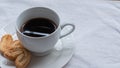 Cup of Greek or Turkish coffee, on small white saucer plate, with two cookie pastries, on white cloth surface