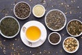 Cup of green tea and bowls of various dried tea leaves on dark, stone background