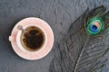 Cup of green tea and decorative peacock feather on concrete background