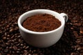 Cup with ground coffee on roasted beans, closeup Royalty Free Stock Photo