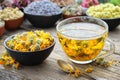 Cup of healthy marigold tea and calendula flowers in bowl. Medicinal herbs - lavender, rose, daisies, Helichrysum on background Royalty Free Stock Photo