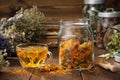 Cup of healthy marigold tea, glass jar of dry calendula flowers. Jars of medicinal herbs and old books on background. Royalty Free Stock Photo